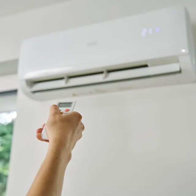 Hånd som bruker fjernkontroll for å justere temperatur på aircondition på veggen.