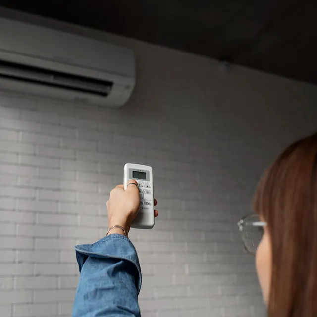 Person som bruker fjernkontroll til å styre aircondition montert på murvegg.